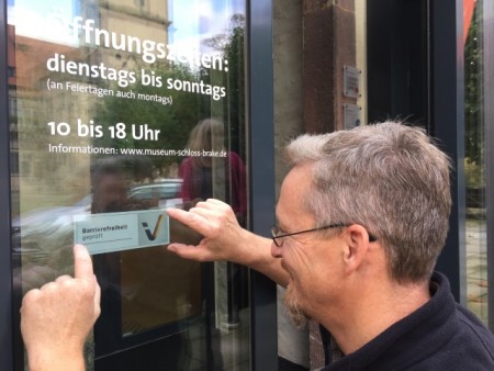Freudestrahlend bringt der Haustechniker Thomas Senke das Schild an der Eingangstür des Weserrenaissance-Museums Schloss Brake an. Foto: Schloss Brake 
