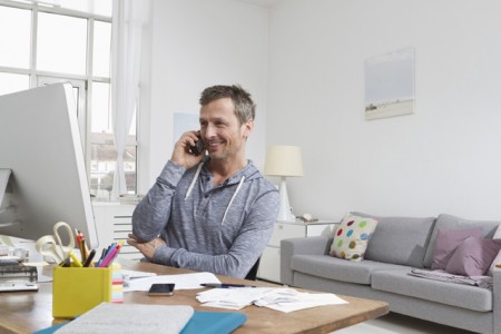 Ein Mann sitzt im Wohnzimmer vor einem Computer und telefoniert