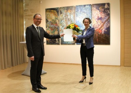  Ministerin Ina Scharrenbach überreicht die Ernennungsurkunde und einen Blumenstrauß an Jörg Düning-Gast, im Hintergrund Werke der ostwestfälischen Künstlerin Rosemarie Sprute.