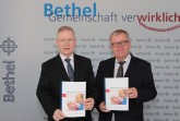 Pastor Ulrich Pohl (r.) und Dr. Rainer Norden mit dem aktuellen BethelJahresbericht 2018/2019. (Foto: Bethel)