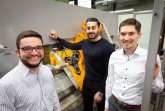 Foto (Fraunhofer IEM): Arbeiten an einem intelligenten Drückwalzprozess: V. l. Julian Rozo Vasquez (WPT, Technische Universität Dortmund), Bahman Arian (LUF, Universität Paderborn) und Markus Riepold (Fraunhofer IEM) vor dem Umform-Prüfstand der Universität Paderborn. Foto: Uni Paderborn