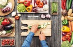 Man cooking and slicing fresh vegetables on a rustic kitchen worktop, healthy eating concept, flat lay