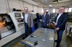Firmenchef Michael Henkenjohann (l.) vor einer modernen CNC-Drehmaschine. Ihm schauen Bürgermeister Michael Berens, in der Hand eine Traverse für Werkzeuge, und Wirtschaftsförderer Thomas Westhof (r.) zu. Foto: Stadt Hoevelhof