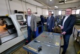 Firmenchef Michael Henkenjohann (l.) vor einer modernen CNC-Drehmaschine. Ihm schauen Bürgermeister Michael Berens, in der Hand eine Traverse für Werkzeuge, und Wirtschaftsförderer Thomas Westhof (r.) zu. Foto: Stadt Hoevelhof