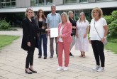 Katja Schultz-Metze (vorne, Mitte) hat im Beisein von Kriminalhauptkommissarin Iris Brinkmann (Kriminalpolizei Gütersloh, vorne, rechts), Ehemann Olaf Metze und ihren drei Kindern Paula (hinten, von links), Lisa und Julia Hufnagel die Ehrenurkunde über die Belobigung des Landes Nordrhein-Westfalen von Regierungspräsidentin Judith Pirscher (vorne, links) entgegengenommen.