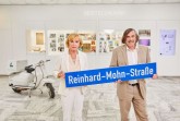 Liz Mohn und Bürgermeister Norbert Morkes bei der Straßenschildübergabe im Bertelsmann Corporate Center. Im Hintergrund steht eine Circulo-Lambretta. Auf einem gleichen Modell hatte sich Reinhard Mohn 1962 in Barcelona mit dem ersten Bertelsmann Club-Katalog fotografieren lassen. Bild: Kai Uwe Osterhellweg.Foto:Stadt Gütersloh