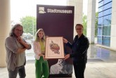 Der Paderborner Künstler Herman Reichold (l.) und seine Assistentin Lara Wenzel übergeben Museumsleiter Markus Runte das erste Exemplar des neuen Libori-Motivs.Foto:© Stadt Paderborn