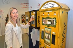 Automatengeschichte zum Anfassen: Annika Maucher an einem Münzautomaten, der Schokolade, Bonbons und Ansichtskarten zur Verfügung stellt. Foto: Automatenmuseum Espelkamp