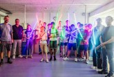 Große Lichtschwertshow in der abgedunkelten Metallwerkstatt: Von links: Dozent Kai Lenski (Argentumsabers), Thomas Mahlmann (zdi-Zentrum Lippe.MINT), links: Dozent Erwin Schadt (Metallwerk OWL/Lippe Bildung eG), dritter von links: Dozent Lukas Dusche (Institut für die Kunststoffwirtschaft/Lippe Bildung eG) mit den stolzen Schülerinnen und Schülern des Lichtschwertkurses. ©Lippe Bildung eG