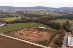 Luftaufnahme der Grabungsfläche für den Neubau des Feuerwehrgerätehauses am Lohagenweg in Hüllhorst. Der Baumbewuchs markiert den Verlauf des Quellbaches, der die Grundlage für die Errichtung der einstigen Hofstelle bildete. Foto: LWL-AfW / A. Koch