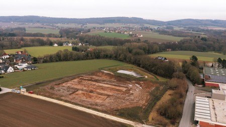 Luftaufnahme der Grabungsfläche für den Neubau des Feuerwehrgerätehauses am Lohagenweg in Hüllhorst. Der Baumbewuchs markiert den Verlauf des Quellbaches, der die Grundlage für die Errichtung der einstigen Hofstelle bildete. Foto: LWL-AfW / A. Koch