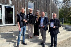 Vor dem Forum Abtei trotzen sie den stürmischen Zeiten: (v.l.) Fotograf und Designer Kalle Noltenhans, Akkordeonist Kamil Dmochowski, Klosterfestival- und Bachwanderung Betreuerin Nicola Nilling, GfW-Geschäftsführer im Kreis Höxter, Michael Stolte, und der künstlerische Leiter der Klosterlandschaft OWL, Hans Hermann Jansen. Foto: Klosterlandschaft OWL/M. Schäfer