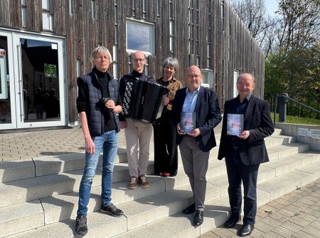 Vor dem Forum Abtei trotzen sie den stürmischen Zeiten: (v.l.) Fotograf und Designer Kalle Noltenhans, Akkordeonist Kamil Dmochowski, Klosterfestival- und Bachwanderung Betreuerin Nicola Nilling, GfW-Geschäftsführer im Kreis Höxter, Michael Stolte, und der künstlerische Leiter der Klosterlandschaft OWL, Hans Hermann Jansen. Foto: Klosterlandschaft OWL/M. Schäfer