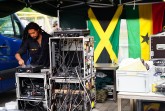 Ein DJ bedient unter einem Pavillon ein Soundsystem mit Plattenspieler und umfangreicher Tontechnik; im Hintergrund hängen die Flaggen Jamaikas und Ghanas.