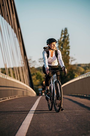 Mitarbeiterin fährt mit Helm auf einem Fahrrad über eine Brücke Bildhinweis: Symbolbild zum Dienstrad-Leasing