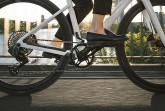 Detailaufnahme eines weißen Fahrrads mit Kettenantrieb und fahrender Person