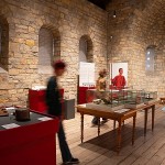 Besucherinnen und Besucher zwischen Vitrinen und Ausstellungsstücken in einem historischen Raum der Kaiserpfalz