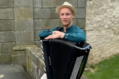 Kamil Dmochowski mit Akkordeon vor einer Steinmauer im Freien