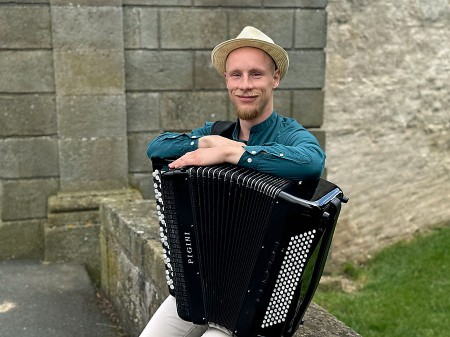 Kamil Dmochowski mit Akkordeon vor einer Steinmauer im Freien