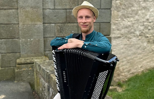 Kamil Dmochowski mit Akkordeon vor einer Steinmauer im Freien