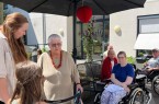 Seniorinnen und Senioren sowie Kinder treffen sich im Garten eines Pflegeheims unter einem Sonnenschirm