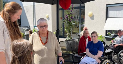 Seniorinnen und Senioren sowie Kinder treffen sich im Garten eines Pflegeheims unter einem Sonnenschirm