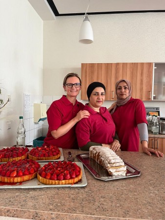 Drei Mitarbeiterinnen präsentieren Erdbeerkuchen und Gebäck in der Küche eines Seniorenheims