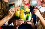 Vier Frauen stoßen mit farbigen Cocktails an, die mit Zitrusfrüchten und kleinen Schirmchen dekoriert sind.