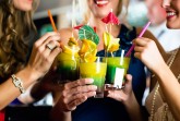 Vier Frauen stoßen mit farbigen Cocktails an, die mit Zitrusfrüchten und kleinen Schirmchen dekoriert sind.