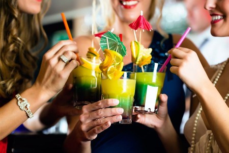 Vier Frauen stoßen mit farbigen Cocktails an, die mit Zitrusfrüchten und kleinen Schirmchen dekoriert sind.
