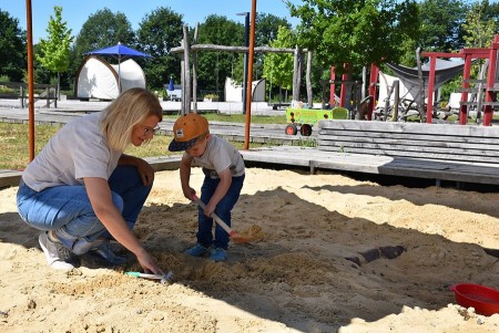 Eine Frau und ein Kind graben gemeinsam mit kleinen Schaufeln in einem Sandkasten im Archäologiepark.