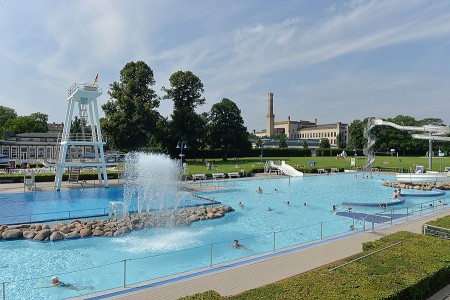 Blick über das Wiesenbad in Bielefeld mit Schwimmbecken, Sprungturm, Wasserrutsche und Badegästen.