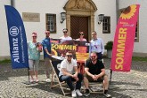 Sieben Beteiligte präsentieren das Plakat zum Open-Air-Sommer in Büren zwischen zwei Veranstaltungsfahnen vor dem Rathaus.