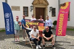 Sieben Beteiligte präsentieren das Plakat zum Open-Air-Sommer in Büren zwischen zwei Veranstaltungsfahnen vor dem Rathaus.