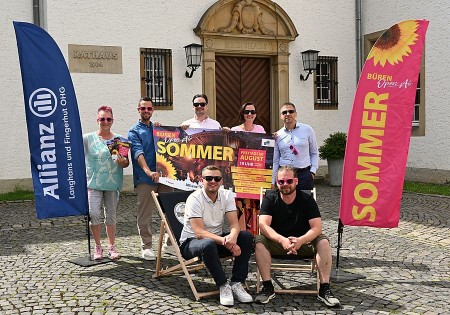 Sieben Beteiligte präsentieren das Plakat zum Open-Air-Sommer in Büren zwischen zwei Veranstaltungsfahnen vor dem Rathaus.