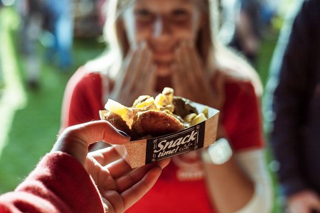 Eine Hand hält eine Schale mit Falafel und weiteren Streetfood-Zutaten, während eine Frau im Hintergrund darauf reagiert