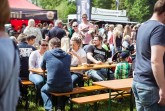 Besucher sitzen und stehen tagsüber zwischen Biertischen und Foodtrucks auf einem Streetfoodfestival.