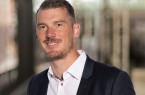 Christopher Boss im dunklen Sakko und weißen Hemd vor einem unscharfen Messehintergrund.