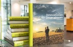 CLAAS Buch „Innovationen für Generationen“ vor mehreren gestapelten Exemplaren auf einem Glastisch.