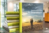 CLAAS Buch „Innovationen für Generationen“ vor mehreren gestapelten Exemplaren auf einem Glastisch.