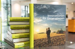 CLAAS Buch „Innovationen für Generationen“ vor mehreren gestapelten Exemplaren auf einem Glastisch.