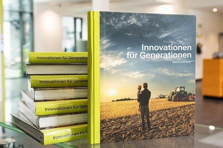 CLAAS Buch „Innovationen für Generationen“ vor mehreren gestapelten Exemplaren auf einem Glastisch.