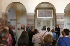 Annika Pröbe führt eine Besuchergruppe im Johanneschor des Westwerks von Corvey und erläutert die historische Inschriftentafel.