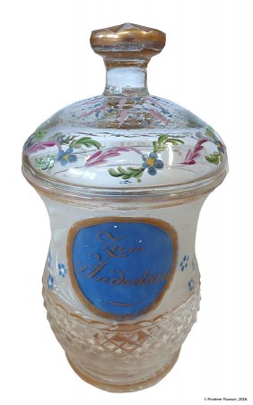 Historischer Deckelbecher aus farblosem Glas mit blauem Medaillon „Zum Andenken“, Blumenmalerei und goldfarbenen Verzierungen.