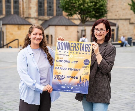 Zwei Frauen halten auf dem Paderborner Domplatz ein Plakat für „Donnerstags in Paderborn“.