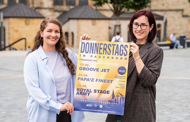 Zwei Frauen halten auf dem Paderborner Domplatz ein Plakat für „Donnerstags in Paderborn“.