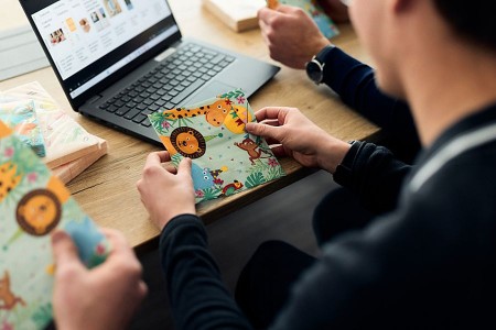 Person hält eine bunt bedruckte Serviette vor einem Laptop während der Analyse der Serviettenproduktion bei Duni.