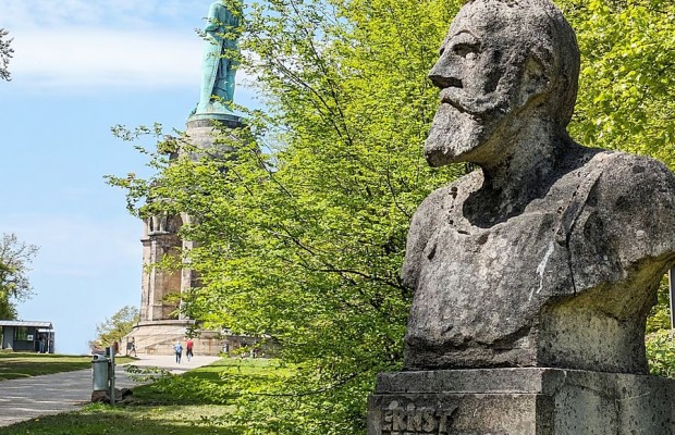 Büste von Ernst von Bandel vor dem Hermannsdenkmal in Detmold, umgeben von grünen Bäumen.