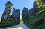 Felsformationen der Externsteine im Sommerlicht mit einem Weg zwischen den Felsen und grüner Vegetation.