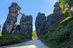 Felsformationen der Externsteine im Sommerlicht mit einem Weg zwischen den Felsen und grüner Vegetation.